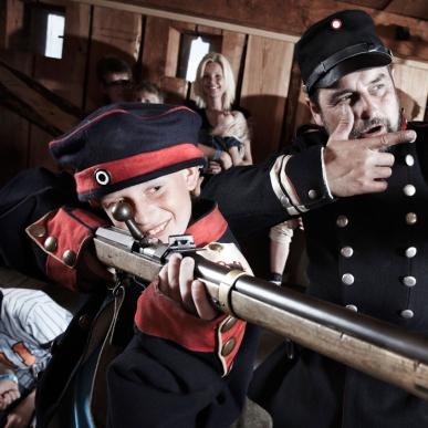 Medarbejder (formidler) og barn i uniform skyder med trægevær på Historiecenter Dybbøl Banke